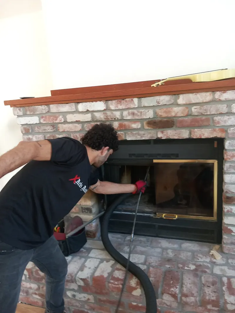 Technician running a HEPA vacuum hose into the fireplace opening during a sweep